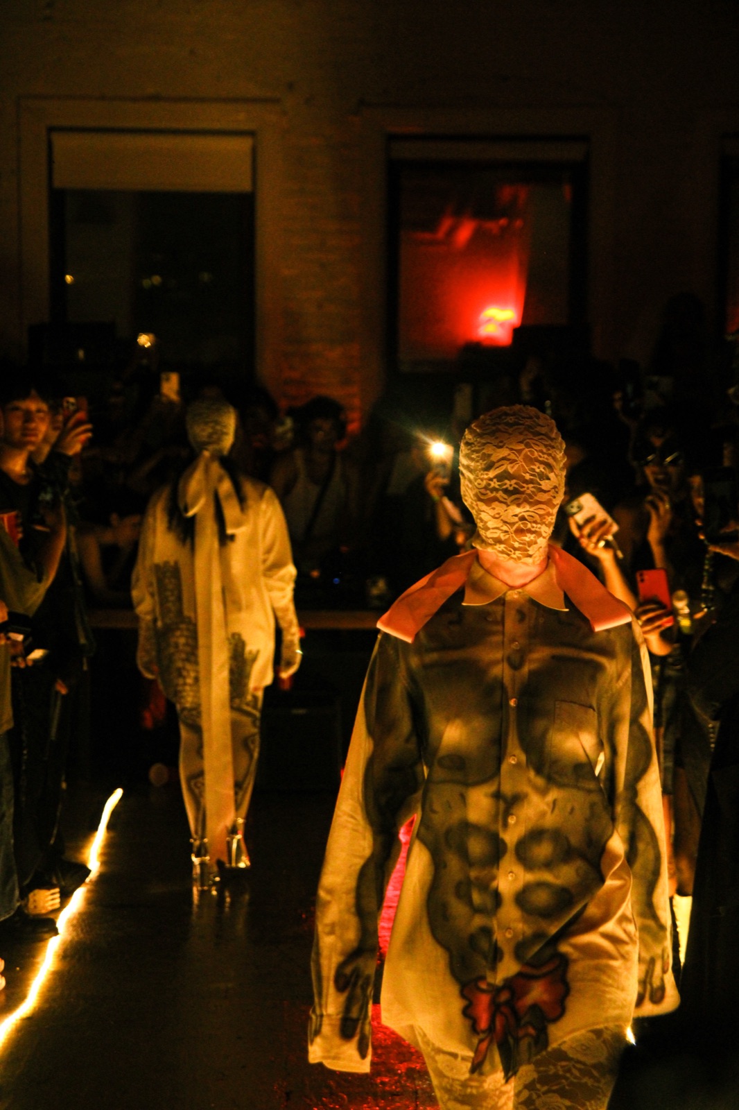 A model in a gold, sculpted bodysuit walks toward the camera between the floor lights.