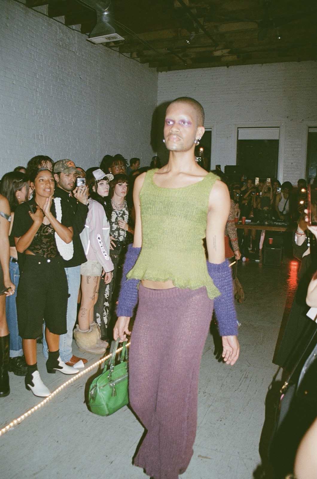 On film: a model in a lime knit top and long mauve skirt walks the runway with the crowd on both sides.