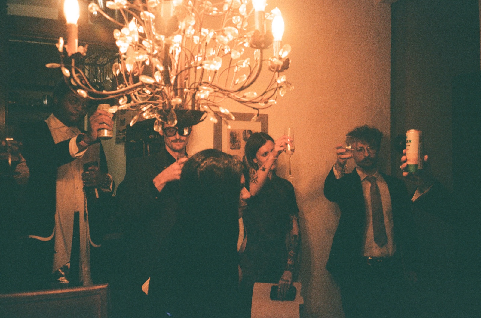 Players in suits and dresses raise their glasses under a candlelit chandelier.