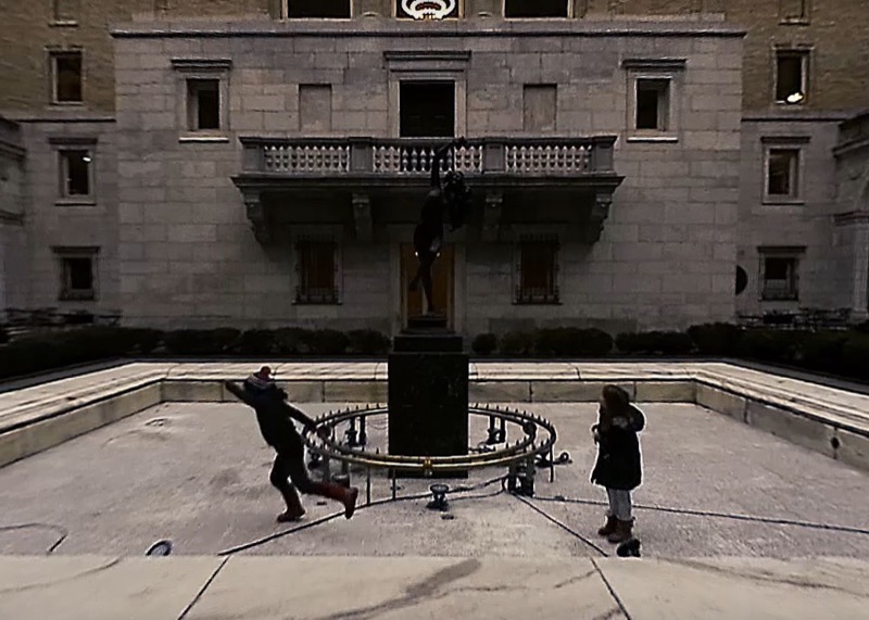 Still from a 360-degree video in the Boston Public Library's courtyard, two figures mid-motion beside a statue.